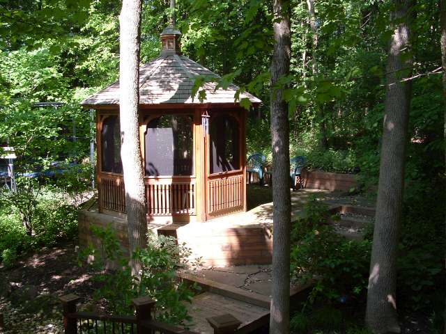 Elevated gazebo in wooded area with stream in background.